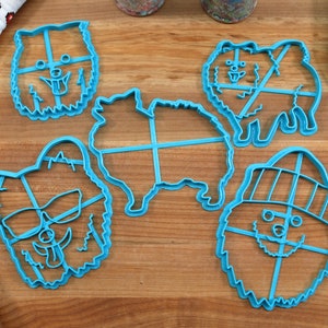 May include: Five blue plastic cookie cutters shaped like Pomeranian dogs. The cutters are on a wooden surface. One cutter has a hat, one has sunglasses, and one is a full body outline.