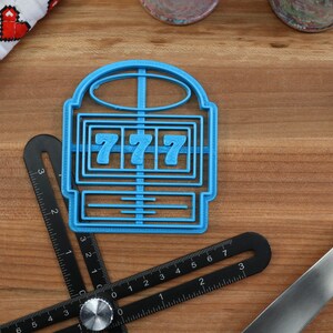 May include: A blue plastic cookie cutter shaped like a slot machine with the number "777" displayed on the reels.