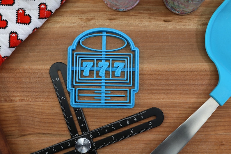May include: A blue plastic cookie cutter shaped like a slot machine with the number "777" displayed on the reels.
