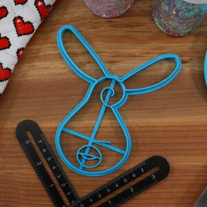 Pu&ograve; includere: Un tagliapasta di plastica blu a forma di coniglio. Il tagliapasta ha un design dettagliato con un piccolo cerchio al centro.