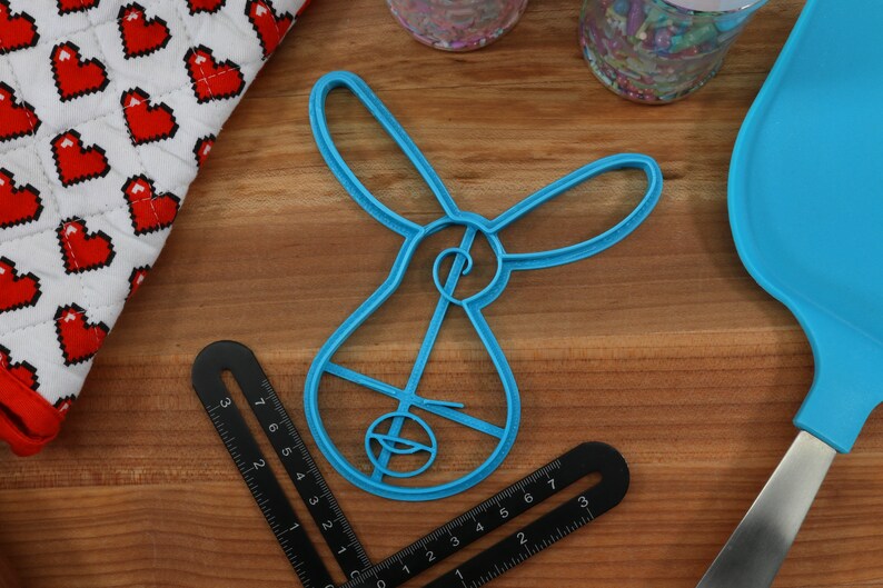 Pu&ograve; includere: Un tagliapasta di plastica blu a forma di coniglio. Il tagliapasta ha un design dettagliato con un piccolo cerchio al centro.