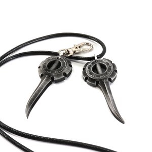 May include: A black leather cord necklace with two silver pendant charms. Each charm features a circular design with a pointed tip.