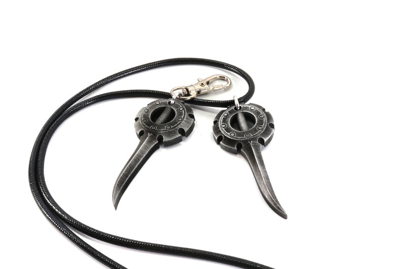 May include: A black leather cord necklace with two silver pendant charms. Each charm features a circular design with a pointed tip.