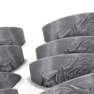 May include: A set of eight grey 3D printed decorative pieces with an intricate design. The pieces are shaped like a curved, flat surface with a raised design.