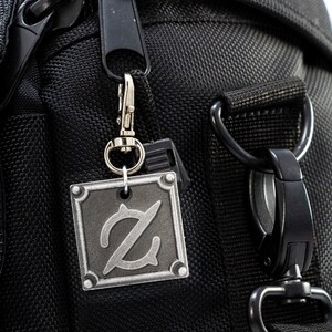 Pu&ograve; includere: Una borsa per fotocamera nera con un portachiavi in metallo argentato che presenta una lettera Z stilizzata.