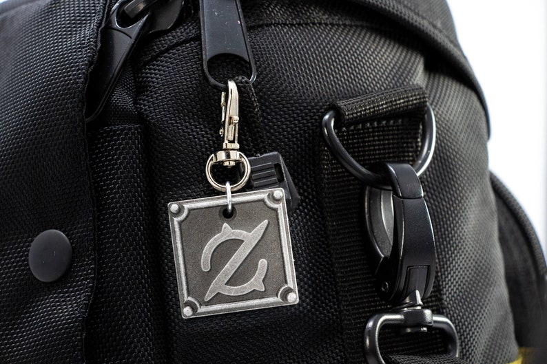 Pu&ograve; includere: Una borsa per fotocamera nera con un portachiavi in metallo argentato che presenta una lettera Z stilizzata.