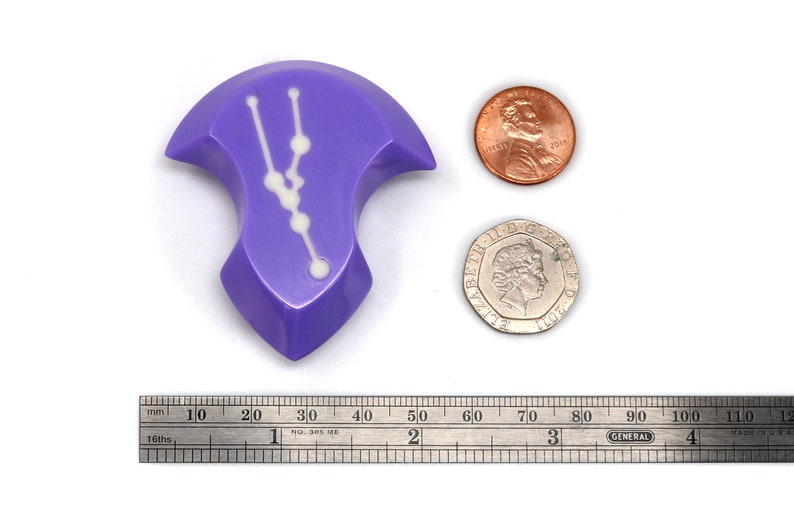 May include: A purple, irregularly shaped dice with a white constellation design. The dice is about the size of a US penny.
