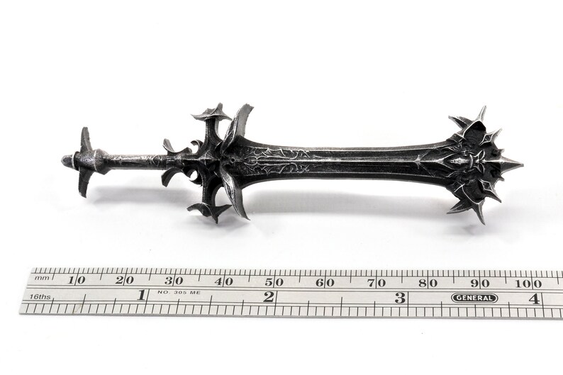 May include: A silver-colored sword with a detailed, intricate design. The sword is approximately 9.5 inches long and has a sharp point. The sword is made of metal and has a textured surface.