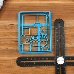 May include: A blue plastic cookie cutter shaped like a cartoon character with a large head and a small body. The cutter is about 2 inches tall and 1.5 inches wide.