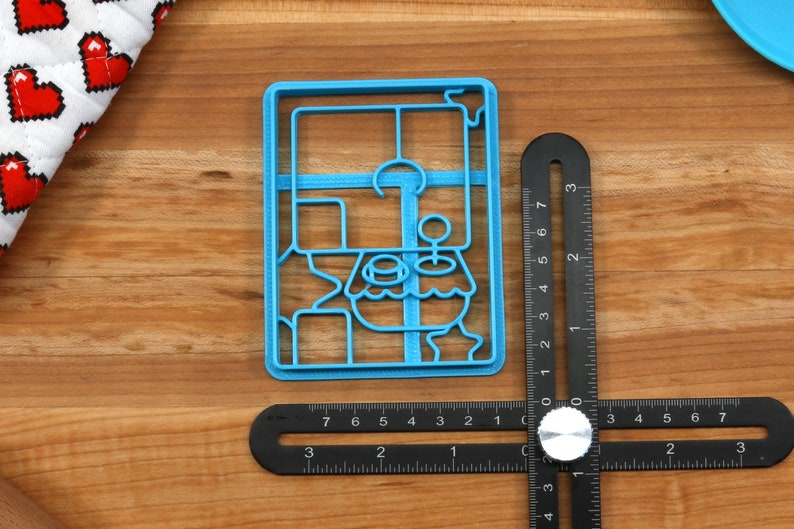 May include: A blue plastic cookie cutter shaped like a cartoon character with a large head and a small body. The cutter is about 2 inches tall and 1.5 inches wide.