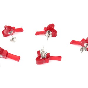 May include: Four pairs of red flower-shaped stud earrings with silver posts. The earrings are displayed on a white background.