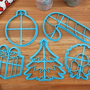 Op de afbeelding: Een set van zes blauwe plastic kerstkoekjesvormen. De vormen zijn in de vorm van een kerstboom, een snoepstok, een cadeau, een ornament en een krans.