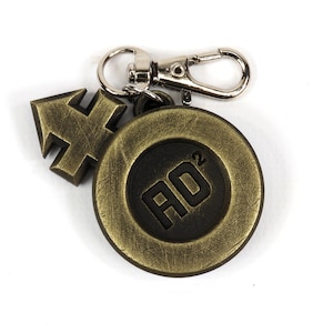 May include: A gold-colored metal keychain with a black circle featuring the text "AO2" and a gold-colored arrow charm.