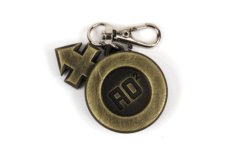 May include: A gold-colored metal keychain with a black circle featuring the text "AO2" and a gold-colored arrow charm.