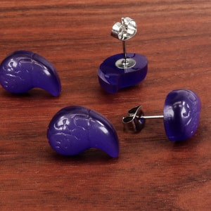 May include: Four purple earrings with a silver post and butterfly design. The earrings are on a wooden surface.