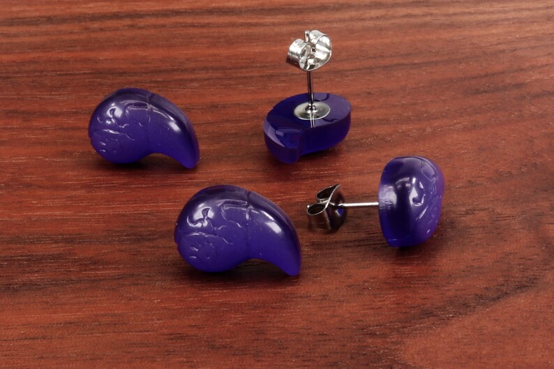 May include: Four purple earrings with a silver post and butterfly design. The earrings are on a wooden surface.