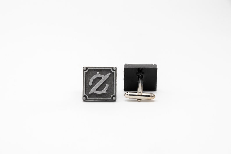 May include: A pair of silver cufflinks with a square design. One cufflink features a stylized letter 'Z' in a silver finish. The other cufflink is black with a silver clasp.