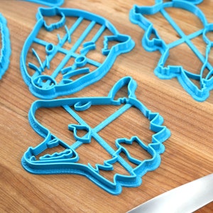 May include: A set of five blue plastic cookie cutters shaped like animal faces. The cutters are on a wooden surface.