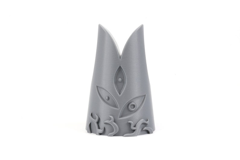 May include: A gray 3D printed crown with a pointed top and three eye-like designs on the front. The crown has a decorative design at the base.