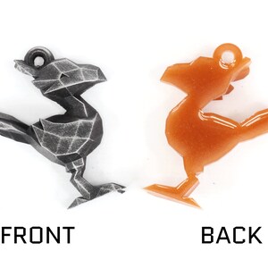 May include: A geometric bird-shaped charm in two finishes: a dark gray with a textured surface and a shiny orange with glitter. The charm has a loop at the top for attaching to a necklace or bracelet.