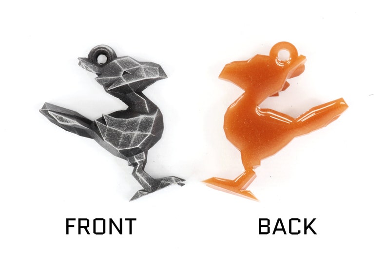 May include: A geometric bird-shaped charm in two finishes: a dark gray with a textured surface and a shiny orange with glitter. The charm has a loop at the top for attaching to a necklace or bracelet.