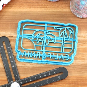 May include: Blue plastic cookie cutter shaped like a California state outline with palm trees and the word "CALIFORNIA" written inside.