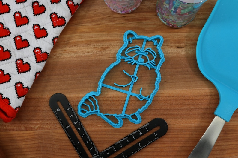 Puede incluir: Un cortador de galletas de pl&aacute;stico azul con forma de mapache. El cortador de galletas est&aacute; sobre una superficie de madera.