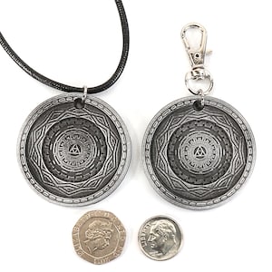 May include: Two silver pendants with a black cord necklace and a silver key chain. The pendants feature a circular design with a triangle inside a circle. The pendants are about the size of a US dime.