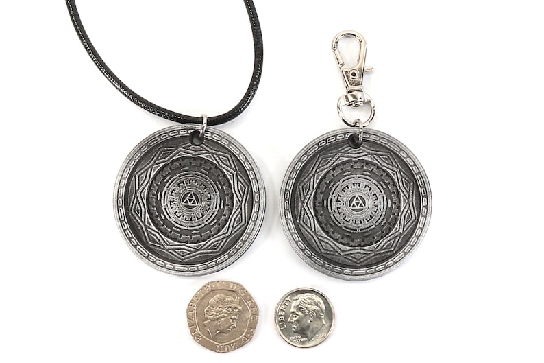 May include: Two silver pendants with a black cord necklace and a silver key chain. The pendants feature a circular design with a triangle inside a circle. The pendants are about the size of a US dime.