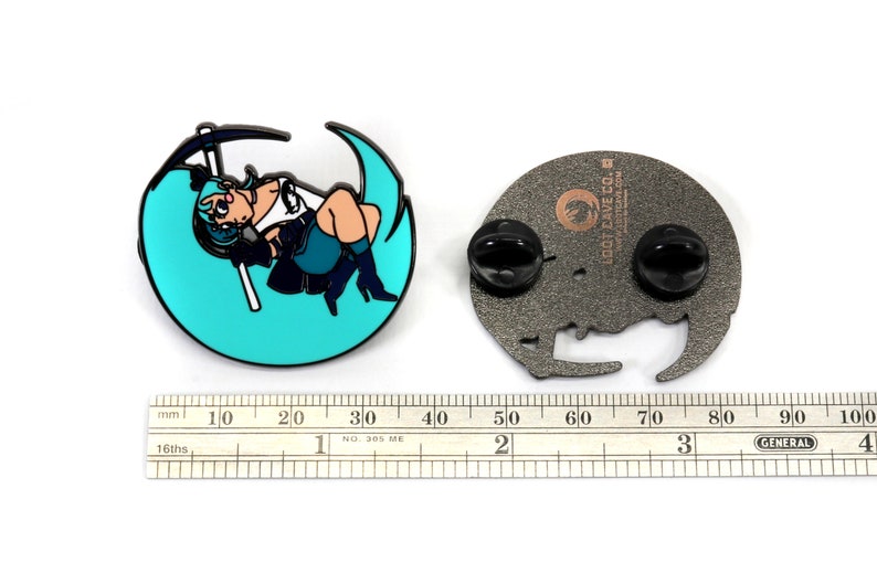 May include: A teal blue enamel pin featuring an anime-style character holding a scythe, sitting on a crescent moon. The pin is attached to a black metal backing with two butterfly clasps. The back of the pin has the text "LOOT CAVE CO. lootcave.com" in a brown font.