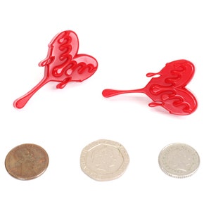 May include: Two red heart-shaped earrings with a dripping design. The earrings are made of plastic and have a shiny finish.