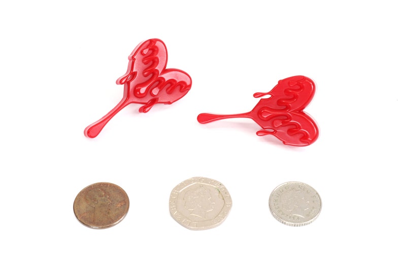 May include: Two red heart-shaped earrings with a dripping design. The earrings are made of plastic and have a shiny finish.