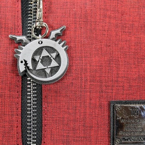 May include: A red zippered bag with a silver metal charm featuring a star and a dragon design. The charm is attached to the zipper pull. The bag has a black zipper and a black patch with the text "Where in the world is Rebecca Google Where" on it.