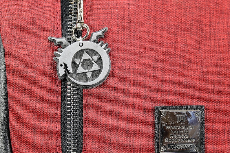 May include: A red zippered bag with a silver metal charm featuring a star and a dragon design. The charm is attached to the zipper pull. The bag has a black zipper and a black patch with the text "Where in the world is Rebecca Google Where" on it.