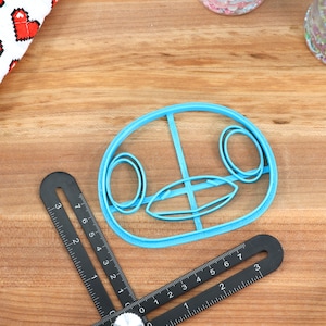 May include: A blue plastic cookie cutter shaped like a cartoon animal face with large eyes and a wide mouth.
