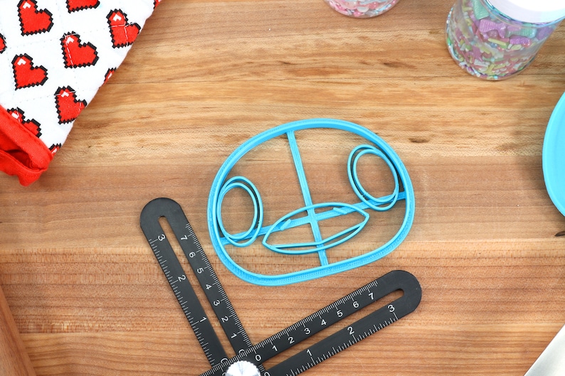 May include: A blue plastic cookie cutter shaped like a cartoon animal face with large eyes and a wide mouth.