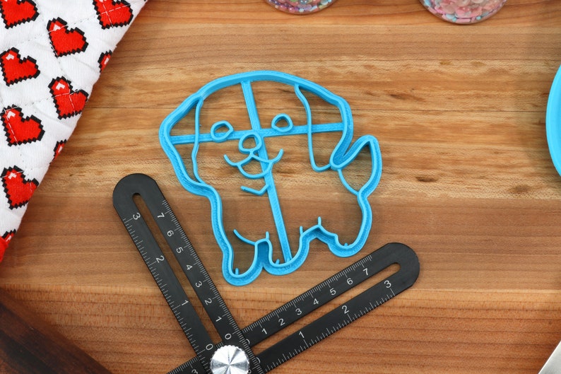 Peut inclure: Un emporte-pi&egrave;ce en plastique bleu en forme de chien. L'emporte-pi&egrave;ce est sur une surface en bois.