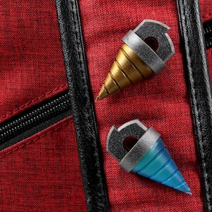 May include: Two miniature drill-shaped accessories, one gold and one blue, with silver accents, rest on a textured red fabric. The accessories have a black top with a hole. A black zipper and trim are visible.