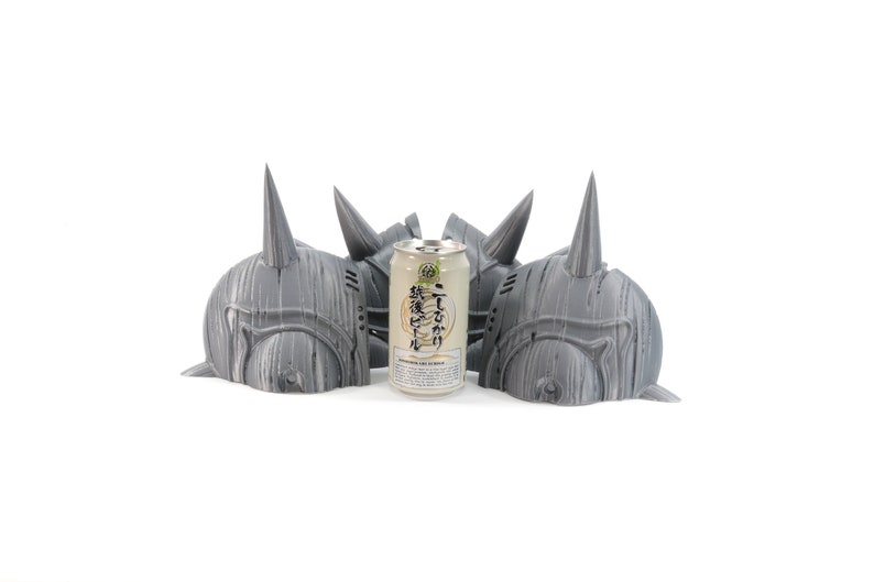 May include: Three gray 3D printed helmets with horns, arranged in a row, with a can of Japanese beer in the center.