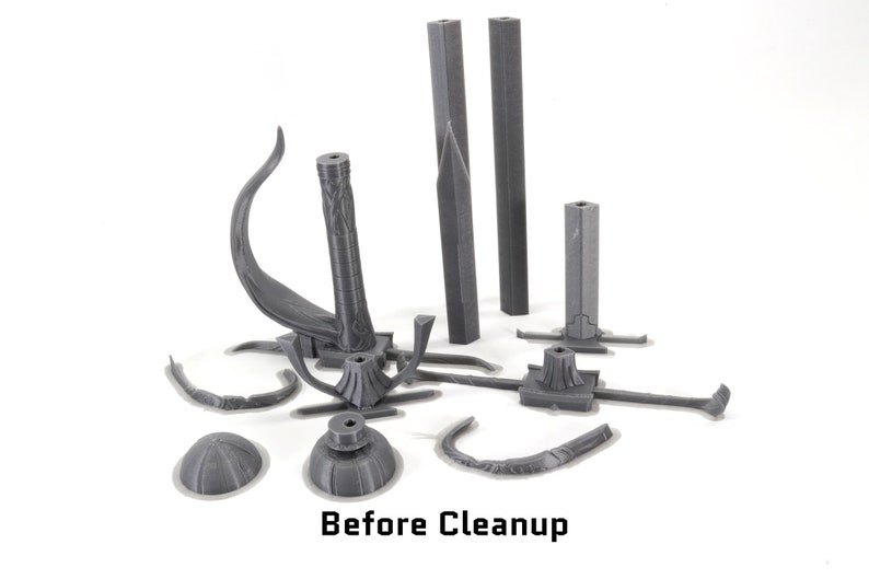 May include: A set of grey 3D printed parts for a model kit. The parts are in various shapes and sizes, including a curved piece, a tall column, and a base with a circular top. The parts are scattered on a white surface. Before Cleanup.