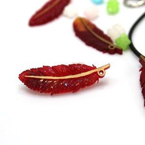 May include: Red and gold feather charm with a glitter finish. The charm has a hole at the top for attaching to a necklace or bracelet.