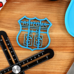 May include: A blue plastic cookie cutter shaped like a vintage Arizona highway sign with the text "Arizona US 66".