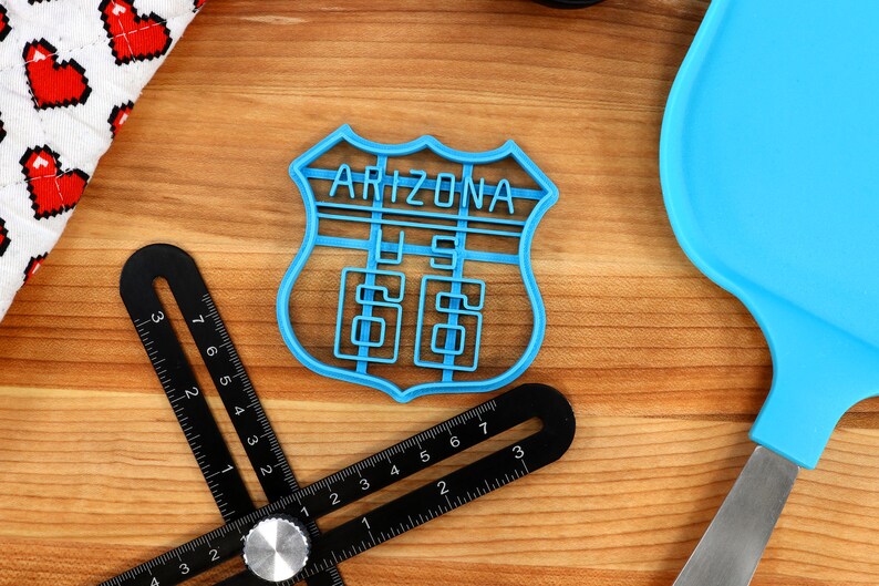 May include: A blue plastic cookie cutter shaped like a vintage Arizona highway sign with the text "Arizona US 66".