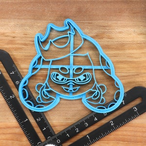 May include: A blue plastic cookie cutter shaped like a cartoon character with a crown, goggles, and tentacles.