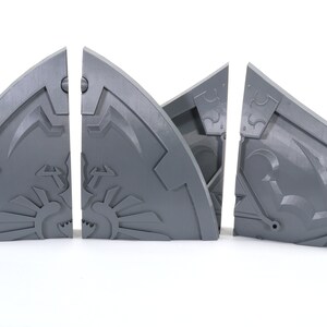 May include: Four gray plastic pieces of a puzzle that form a shield with a design on it.