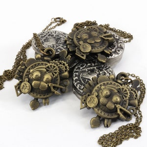 May include: Three gold-toned necklaces with intricate, detailed pendants featuring a cartoon-like face with gears and other mechanical elements. The pendants are attached to chains with a silver-toned coin charm.