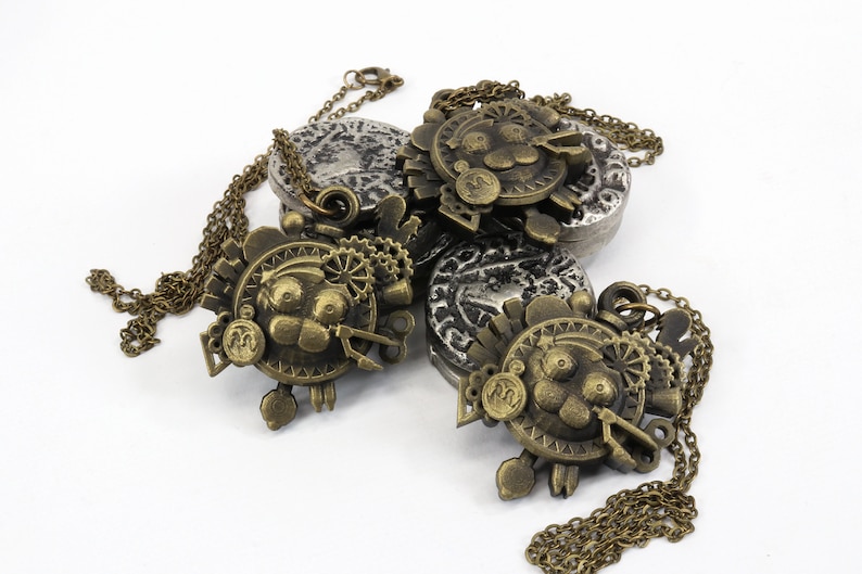 May include: Three gold-toned necklaces with intricate, detailed pendants featuring a cartoon-like face with gears and other mechanical elements. The pendants are attached to chains with a silver-toned coin charm.