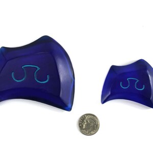 May include: Two blue ceramic dishes with a raised, light blue symbol in the center. The larger dish is slightly curved and the smaller dish is more rounded.