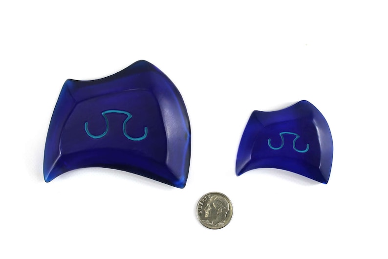 May include: Two blue ceramic dishes with a raised, light blue symbol in the center. The larger dish is slightly curved and the smaller dish is more rounded.