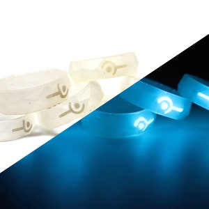 May include: Five white glow-in-the-dark rings with a symbol on each. The rings are stacked on top of each other. The rings are glowing blue in the dark.